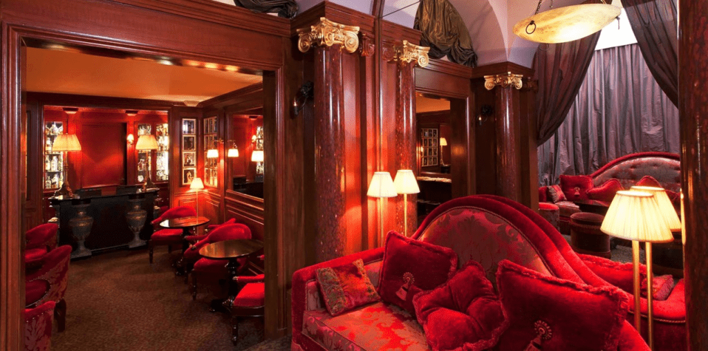 Innenansicht der Red Bar im Hotel Maison Athénée Paris – edles Interieur mit roten Samtsofas, warmem Licht und klassischem Pariser Dekor von Jacques Garcia
